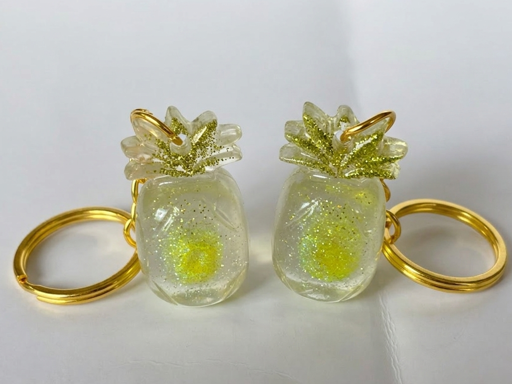 Two pineapple-shaped keychains with gold rings on a white background