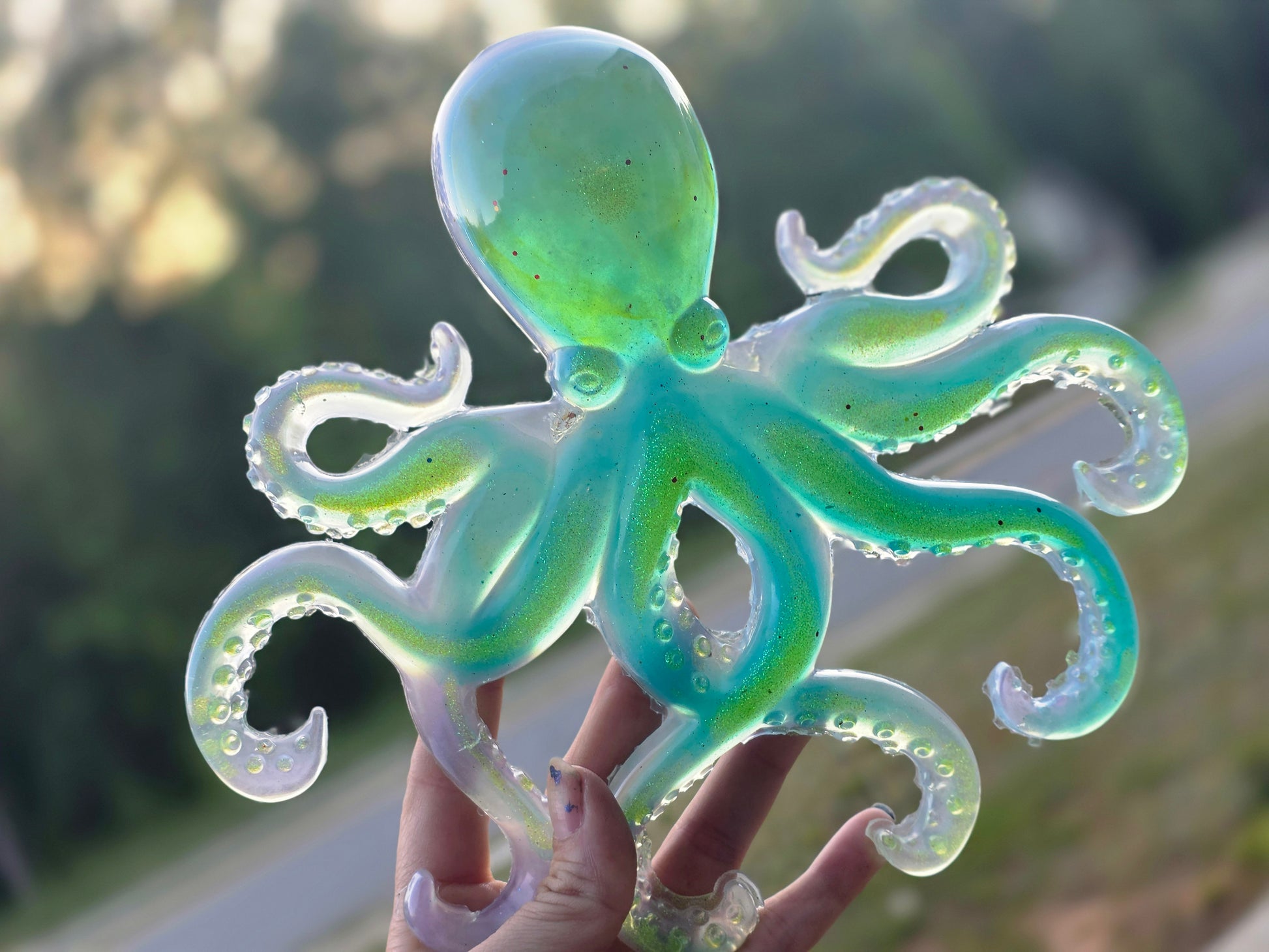 Transparent octopus toy held by a hand with a blurred outdoor background
